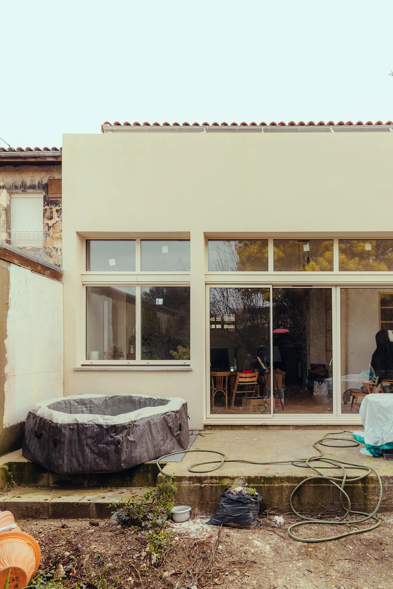 Vue de la façade arrière avec sa grande baie double hauteur, 4 ouvrants sur terrasse, linteau, maçonnerie et enduit ton pierre, menuiserie en alu couleur beige